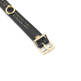 Close-up view of black leather Shining Girl ankle cuff with golden buckle and green gem embellishments on a white background