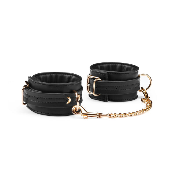 Black vegan leather handcuffs with gold hardware and D-rings, part of the Dark Candy collection, suitable for bondage play