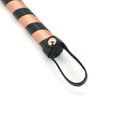 Close-up of rose gold and black leather flogger handle, stylish accessory for BDSM impact play