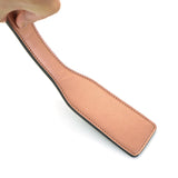 Hand holding a rose gold leather spanking paddle, designed for luxury impact play, from the Rose Gold Memory collection