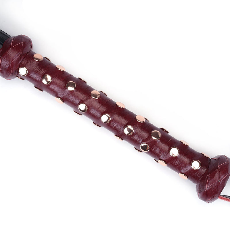 Close-up of a wine red leather flogger handle with rose gold studs, part of a luxurious bondage accessory collection