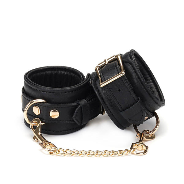 Luxurious black leather bondage wrist cuffs with gold chain and buckles from Dark Secret collection