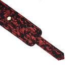 Close-up of Victorian Garden lace and vegan leather handcuff with brass snap, showcasing intricate red and black design for BDSM play