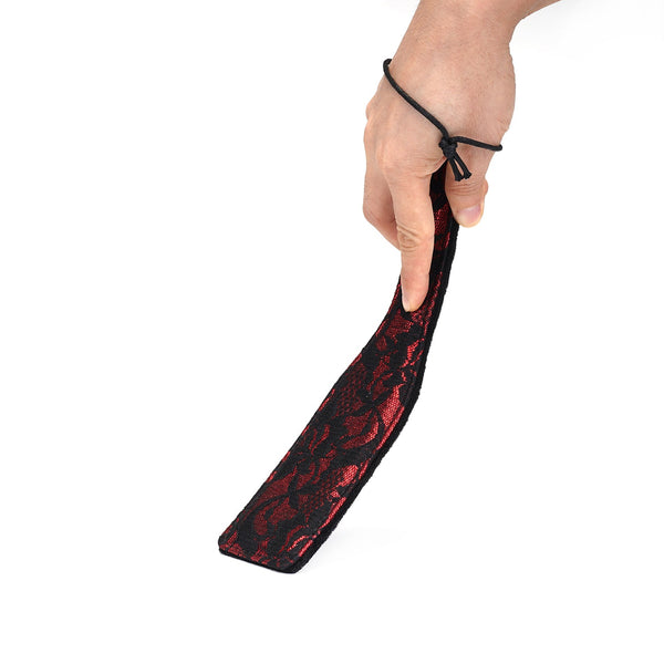 Hand holding Victorian Garden dual-texture BDSM spanking paddle with black and red lace design and wrist loop