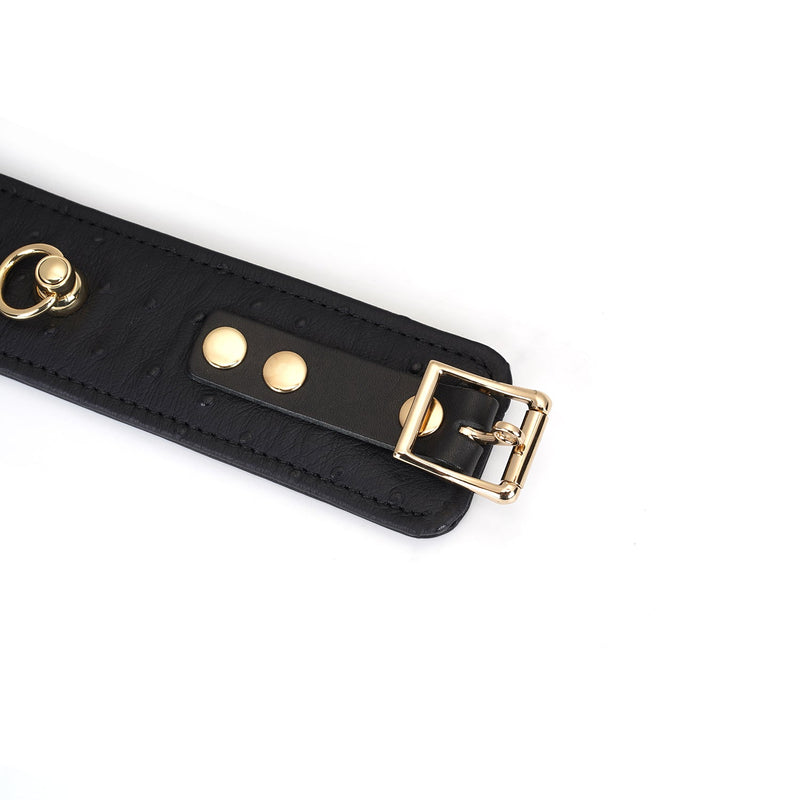 Black leather handcuff with ostrich skin pattern and gold buckle and D-ring, part of the Demon's Kiss BDSM collection
