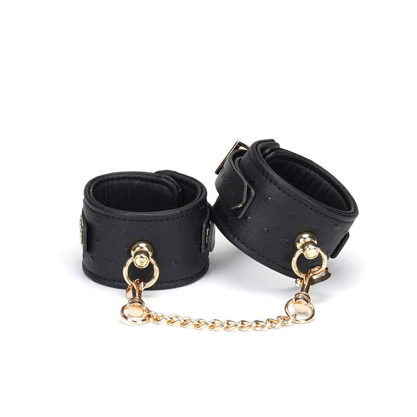 Black leather handcuffs with ostrich skin pattern and gold chain from Demon's Kiss Collection, showcasing premium BDSM wrist restraints