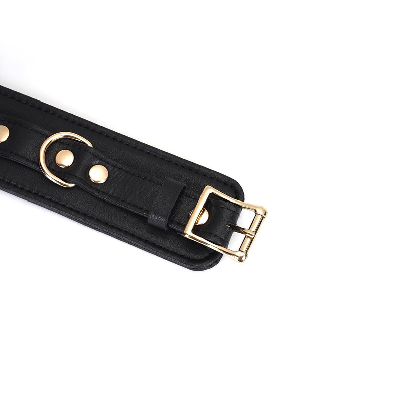 Close-up of black leather bondage ankle cuff with gold buckle and hardware, designed for restraint play compatibility with spreader bars and other accessories
