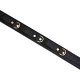 Close-up view of black leather thigh cuffs with gold hardware, adjustable holes for restraint play from the Dark Secret collection