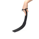 Hand holding Dark Secret Dual Sensation Leather Spanking Paddle for BDSM play, showing the textured black leather and curve design