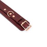 Close-up of wine red leather handcuffs with rose gold buckle and hardware, showcasing luxurious craftsmanship and design for bondage play