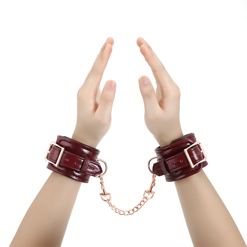 Wine red leather handcuffs with rose gold hardware worn on hands posed in a V shape, exemplifying luxurious bondage wrist restraints