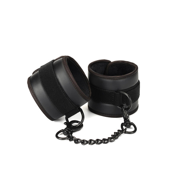 Black faux leather wrist cuffs with plush padding and quick-release chain, suitable for vegan-friendly bondage play