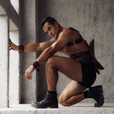 Man in fetishwear from The Equestrian collection featuring bondage cuffs and vintage gold hardware in a moody industrial setting