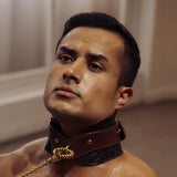 Man wearing premium leather posture collar and chain leash from The Equestrian collection, with detailed golden hardware and quilted leather design