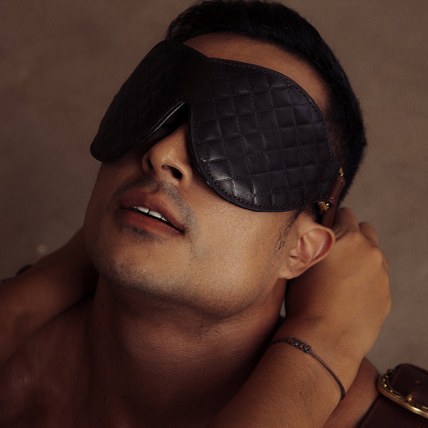 Man wearing a quilted leather bondage blindfold from The Equestrian collection, featuring vintage gold hardware, enhancing sensory deprivation play