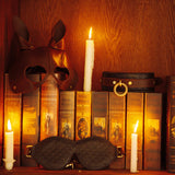 Luxurious BDSM accessories including a leather rabbit mask, quilted blindfold, and vintage gold collar displayed on a bookshelf with candlelight, symbolizing sophisticated sensory play and bondage elegance
