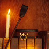 Luxury leather riding crop from The Equestrian collection, presented with vintage books and a lit candle for sophisticated bondage play