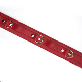 Close-up of red faux leather wrist to thigh cuffs with metal eyelets for adjustable fit, part of bondage kit