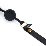 Demon's Kiss breathable silicone ball gag with black leather strap and gold hardware, showcasing luxurious bondage accessory design