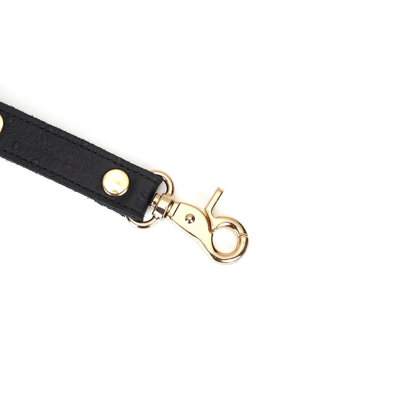 Close-up of black leather hog tie with ostrich skin pattern and gold clip, part of the Demon's Kiss bondage collection