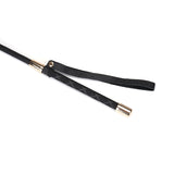 Black leather BDSM riding crop with heart-shaped tip and wrist loop, showcasing textured handle and gold metal accents for luxurious bondage play